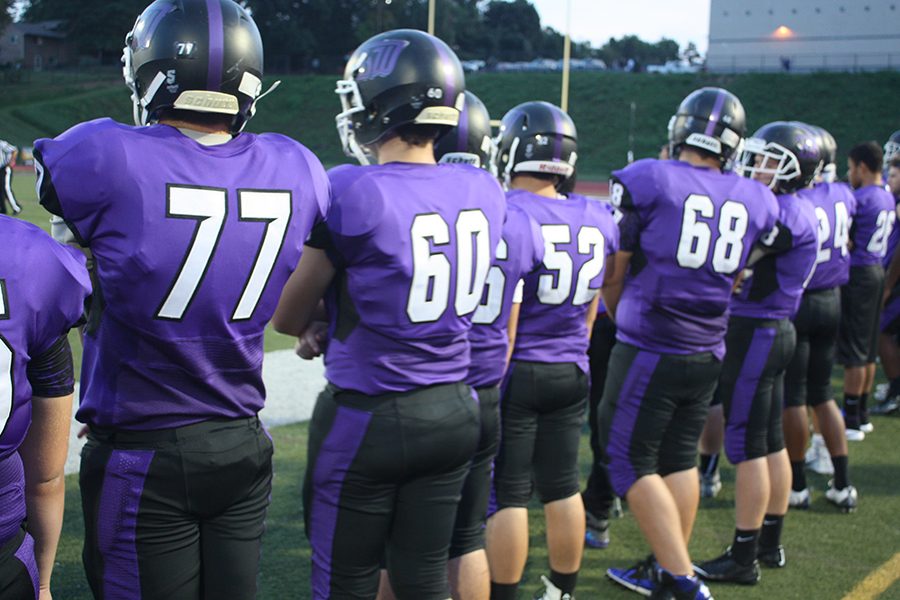 Varsity football players stand by, ready for action on the sidelines. 