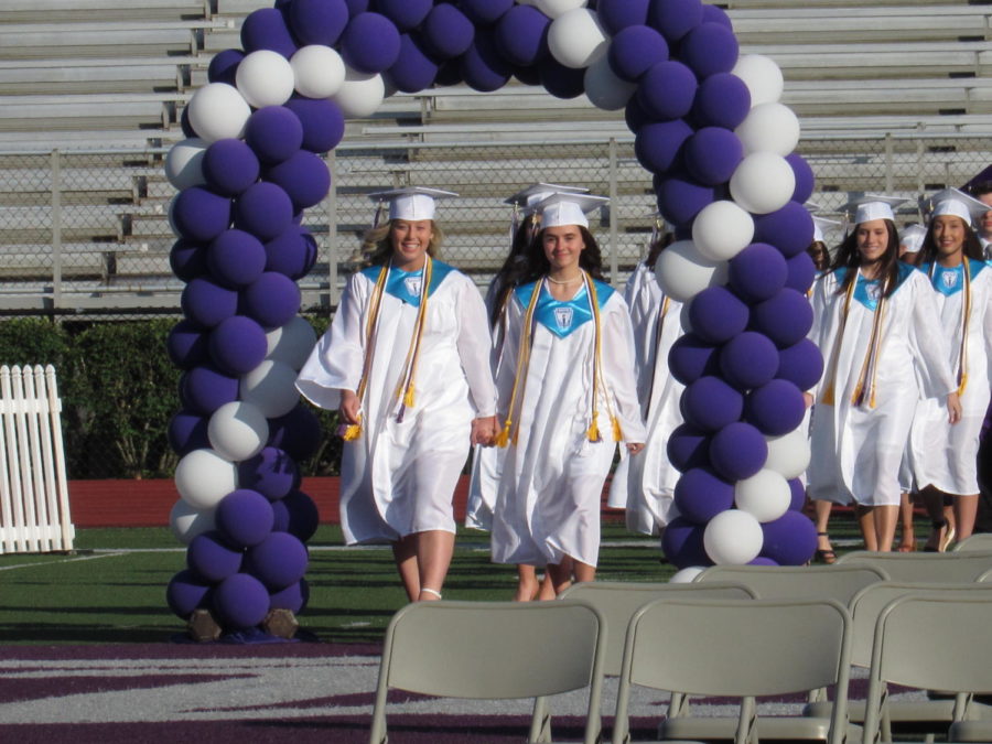 Seniors walk down the football field side by side before graduating. 