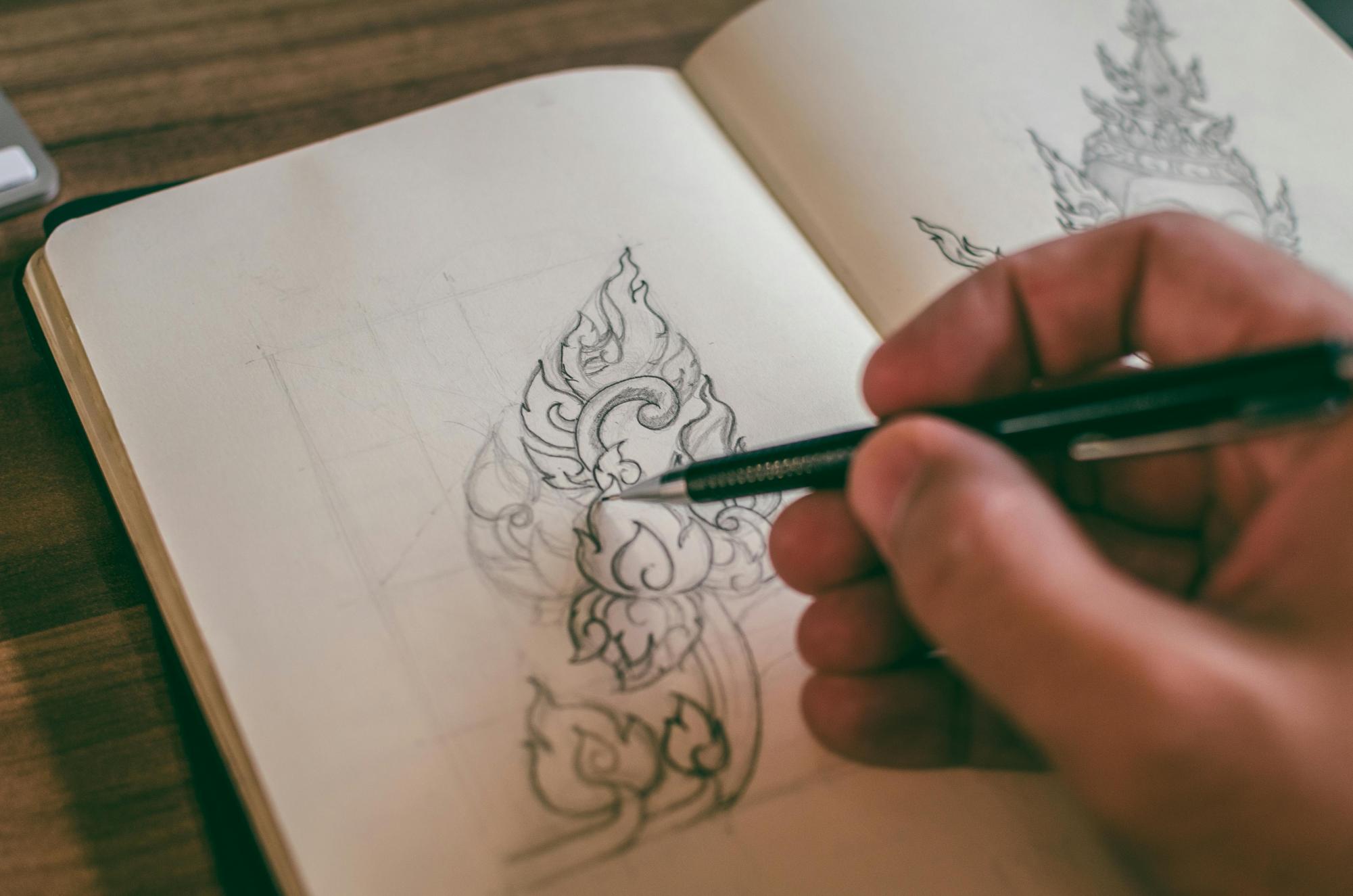 An artist draws on a sketchpad with a pencil. Image via Pexels by Pixabay. 