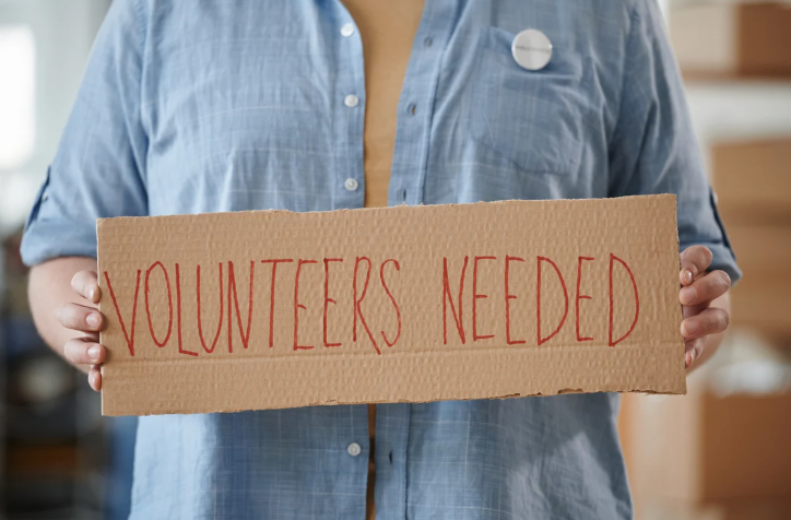 Person holding a sign reading 'Volunteers Needed' to encourage community support. Image via Pexels.